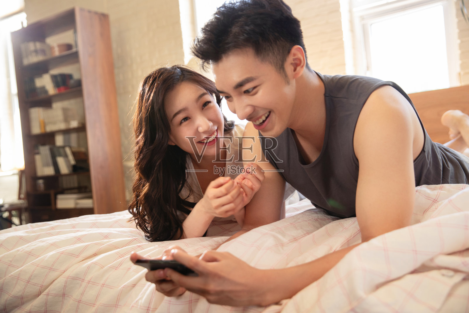 青年情侣趴在床上玩手机照片摄影图片