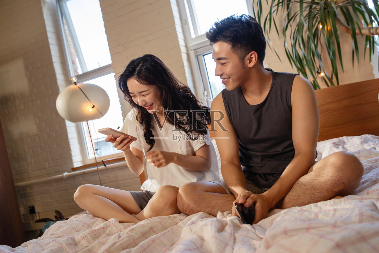 青年情侣趴在床上玩手机照片摄影图片