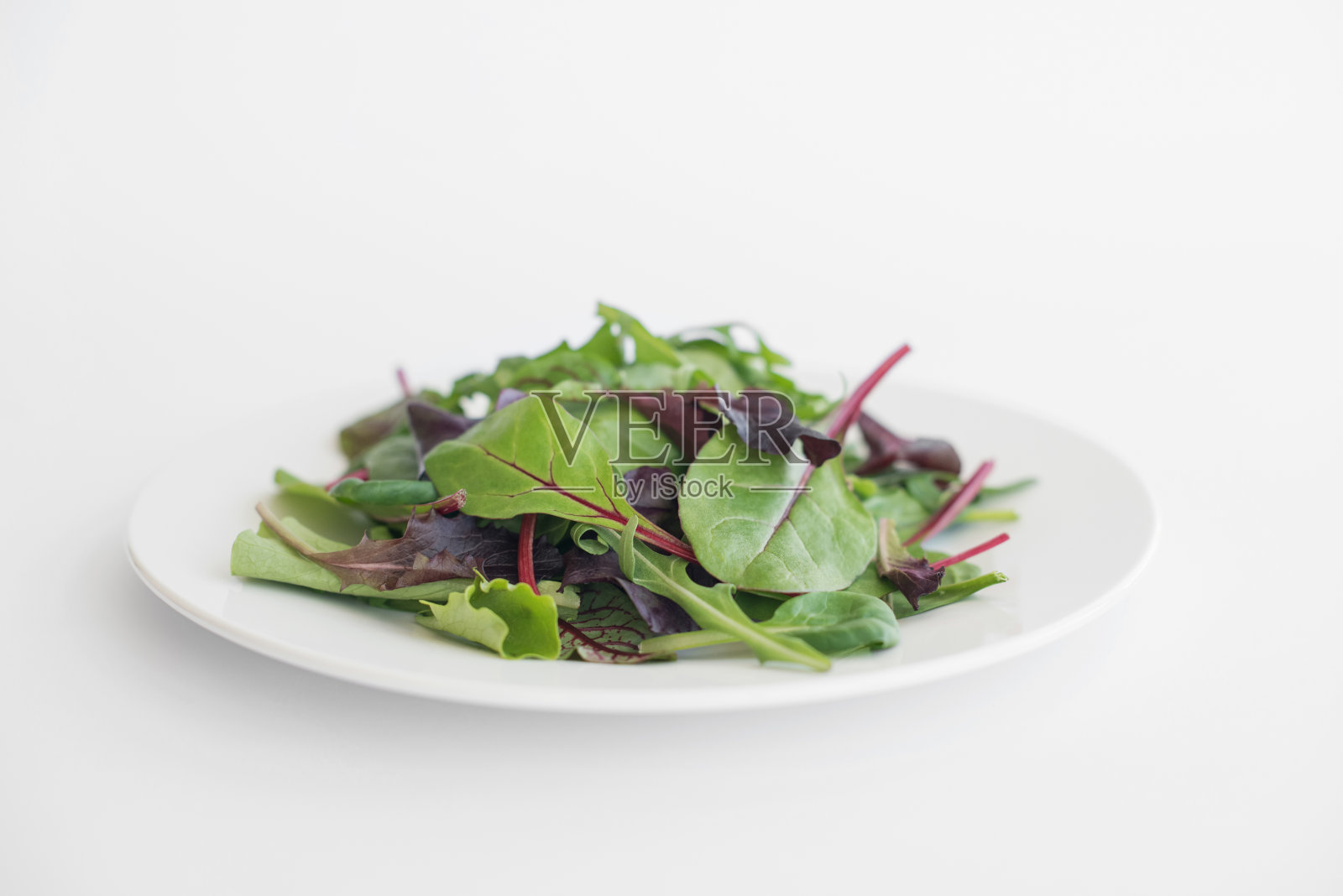 绿叶菠菜,芝麻菜,生菜放在白色的盘子里,放在白色的桌子上照片摄影图片