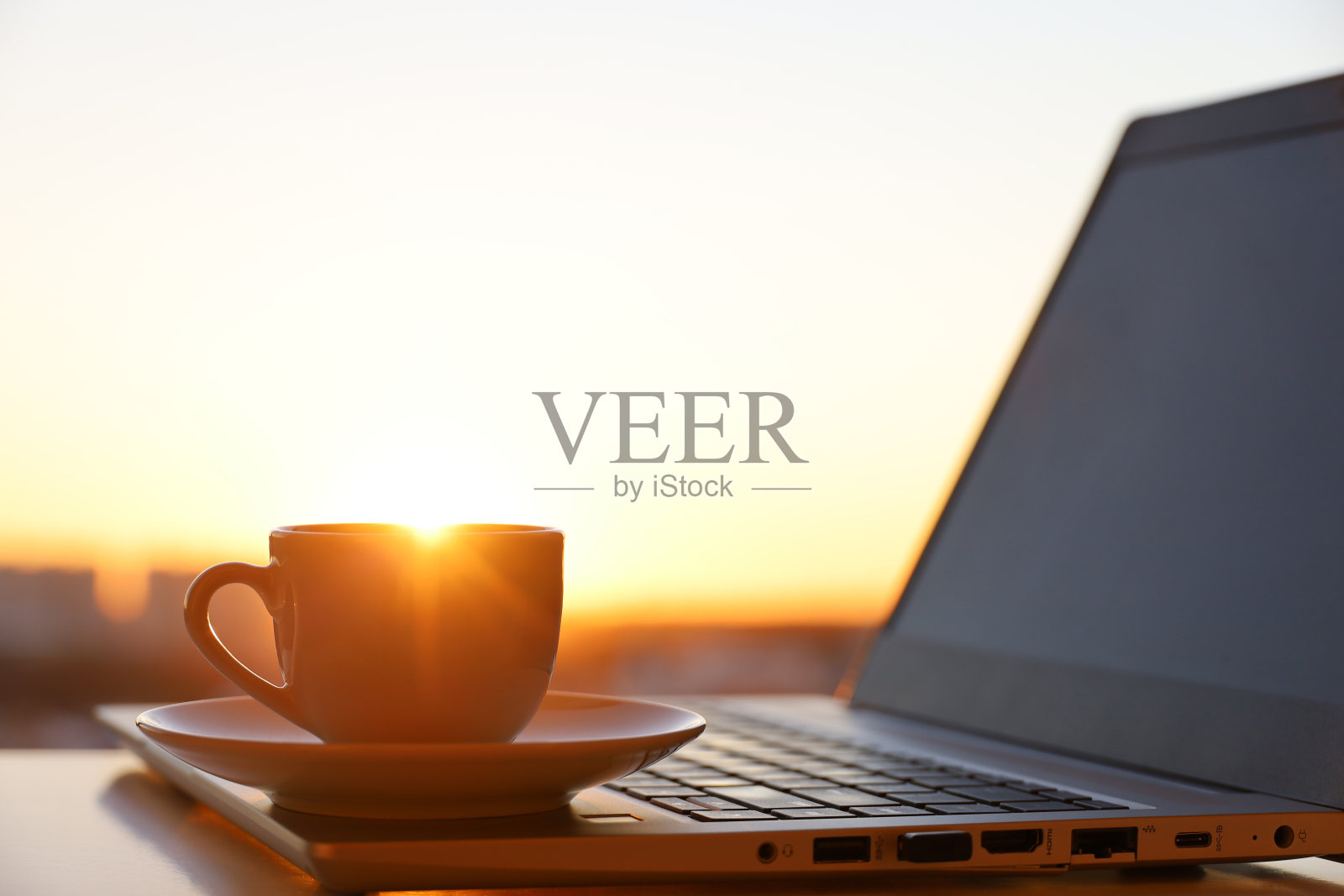 把咖啡或茶杯放在笔记本电脑上,靠在阳光下的窗户上照片摄影图片