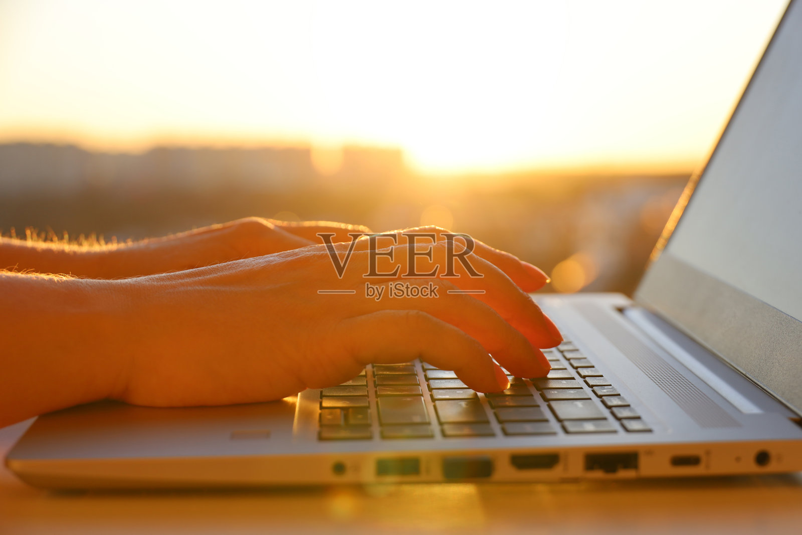 女性的手放在笔记本电脑键盘上,靠近阳光的窗户照片摄影图片