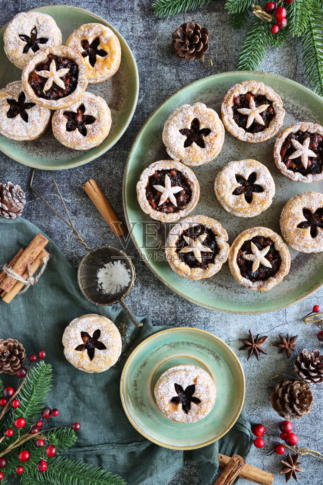 绿色盘子上自制的肉馅饼,上面撒着糖霜,节日的圣诞甜点酥皮,甜肉馅,云杉针,红色浆果,松果,筛子,薄纱,高架的画面照片摄影图片