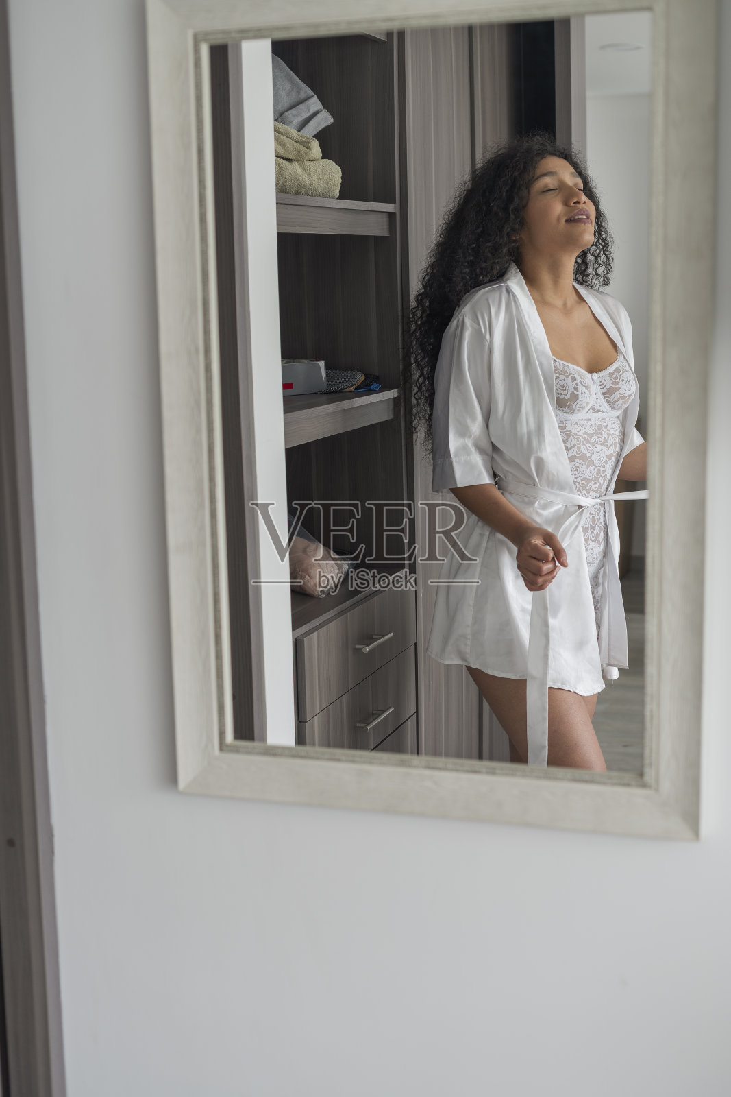 留着非洲式发型的拉丁女子穿着睡衣和丝绸长袍,站在自家的化妆间里对着镜子照片摄影图片