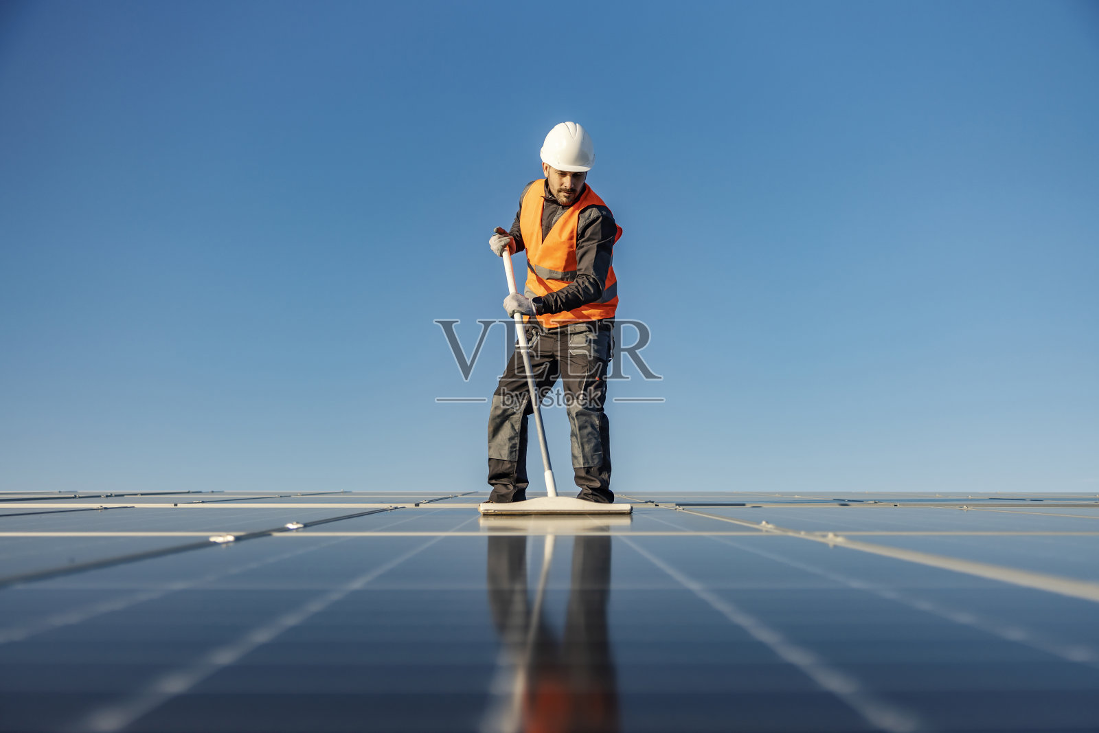 一个杂工用扫帚在屋顶上刷太阳能电池板。照片摄影图片