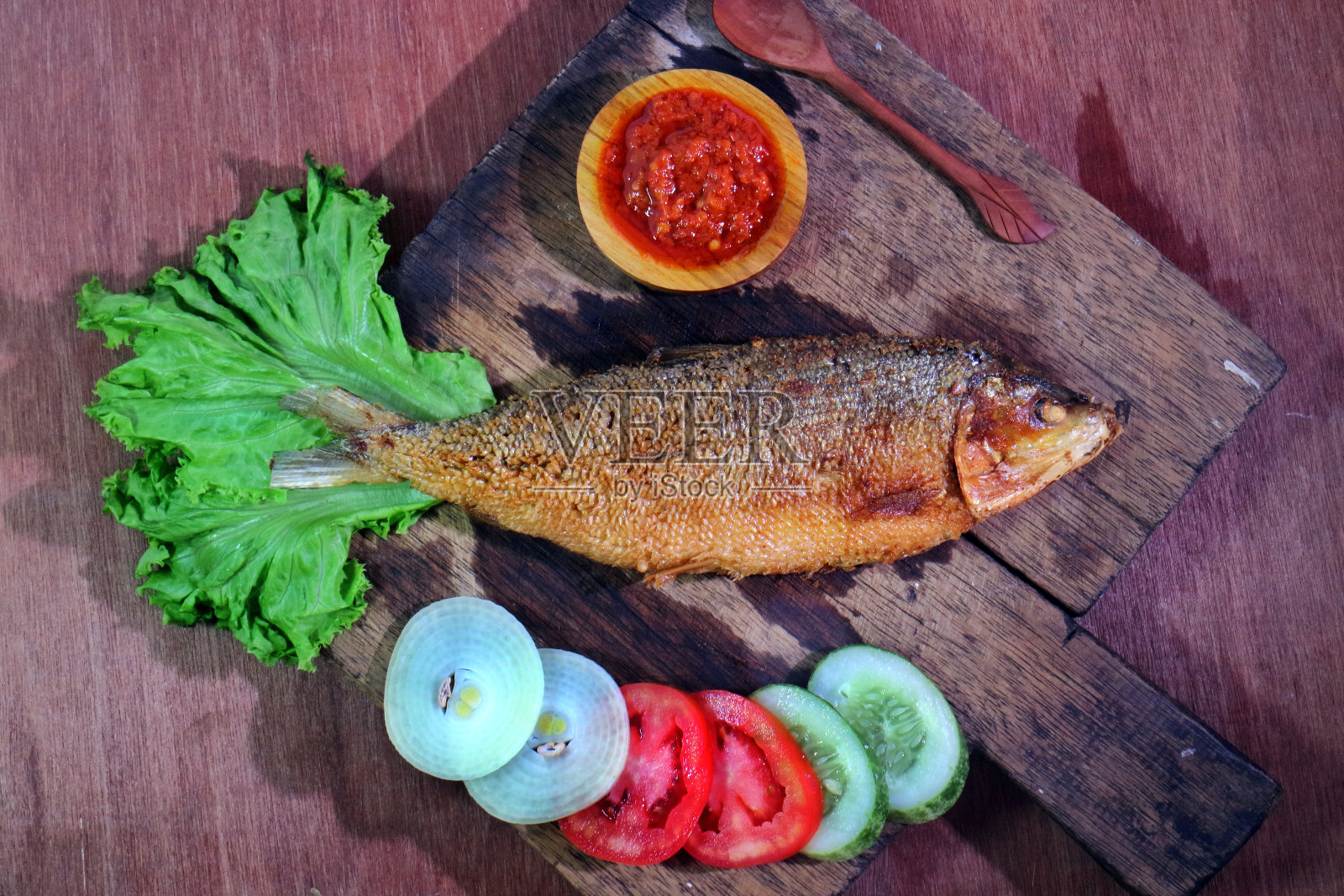 在切菜板上煎炸斑鱼,配上沙拉洋葱、黄瓜、西红柿和辣椒酱照片摄影图片