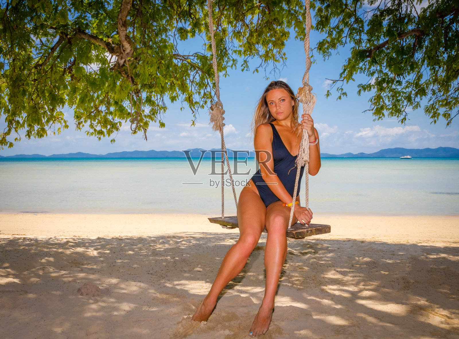 一个穿着泳衣的小女孩在海边荡秋千。对着镜头摆姿势。照片摄影图片