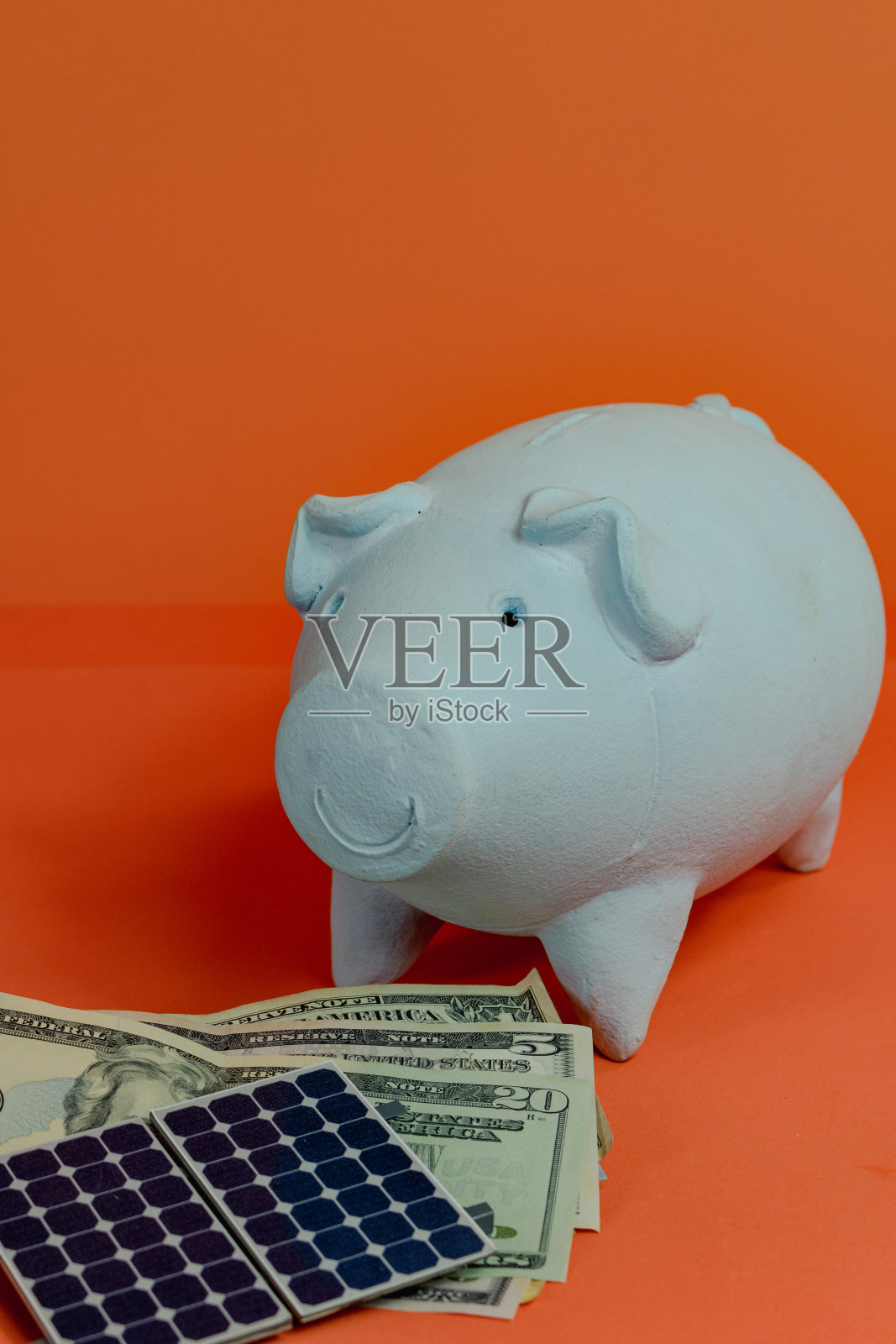 储蓄罐与美元和光伏太阳能电池板隔离在橙色背景。照片摄影图片