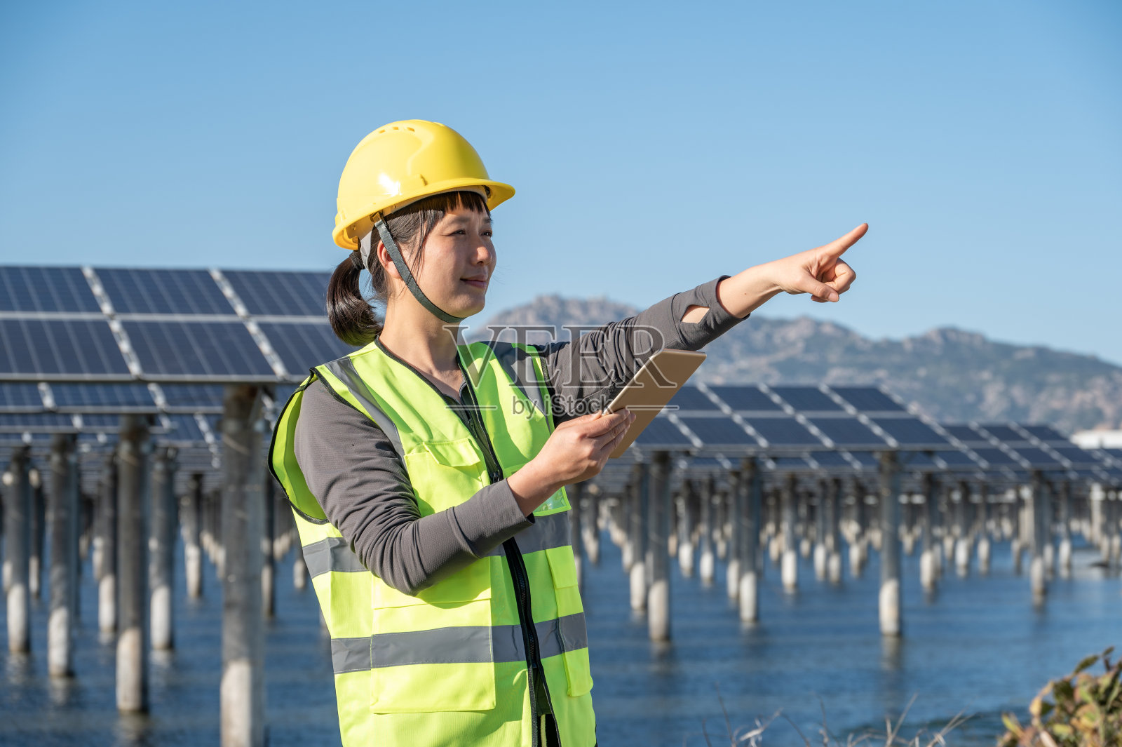 在蓝天下,一位亚洲妇女在海边的光伏太阳能电站用平板电脑工作照片摄影图片