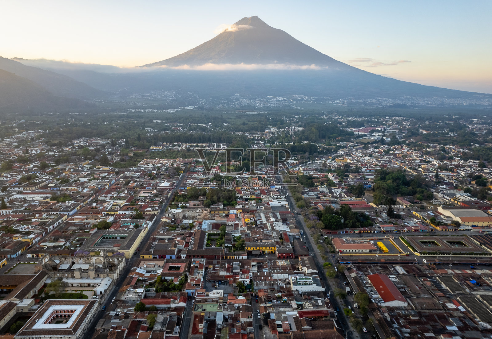 在阳光明媚的一天,危地马拉安提瓜岛,可以看到死气沉沉的阿瓜火山、鹅卵石街道和屋顶照片摄影图片