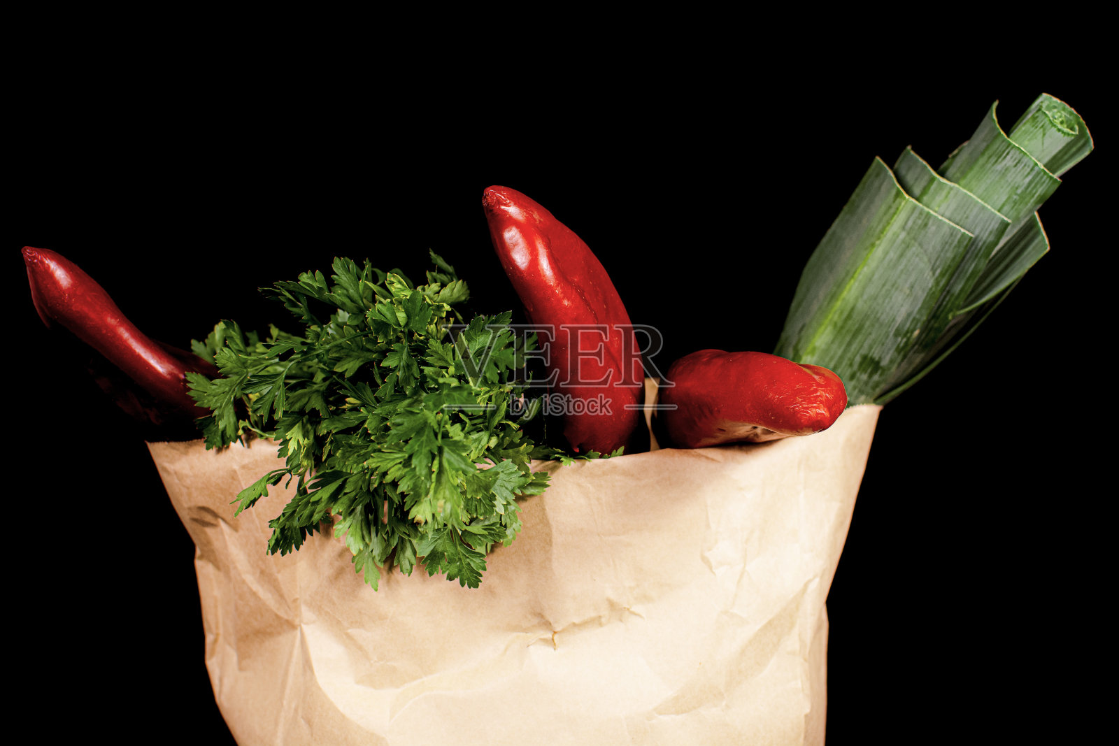 带新鲜蔬菜的纸袋。韭葱,红甜椒,欧芹放在一个黑色背景的纸袋里。照片摄影图片