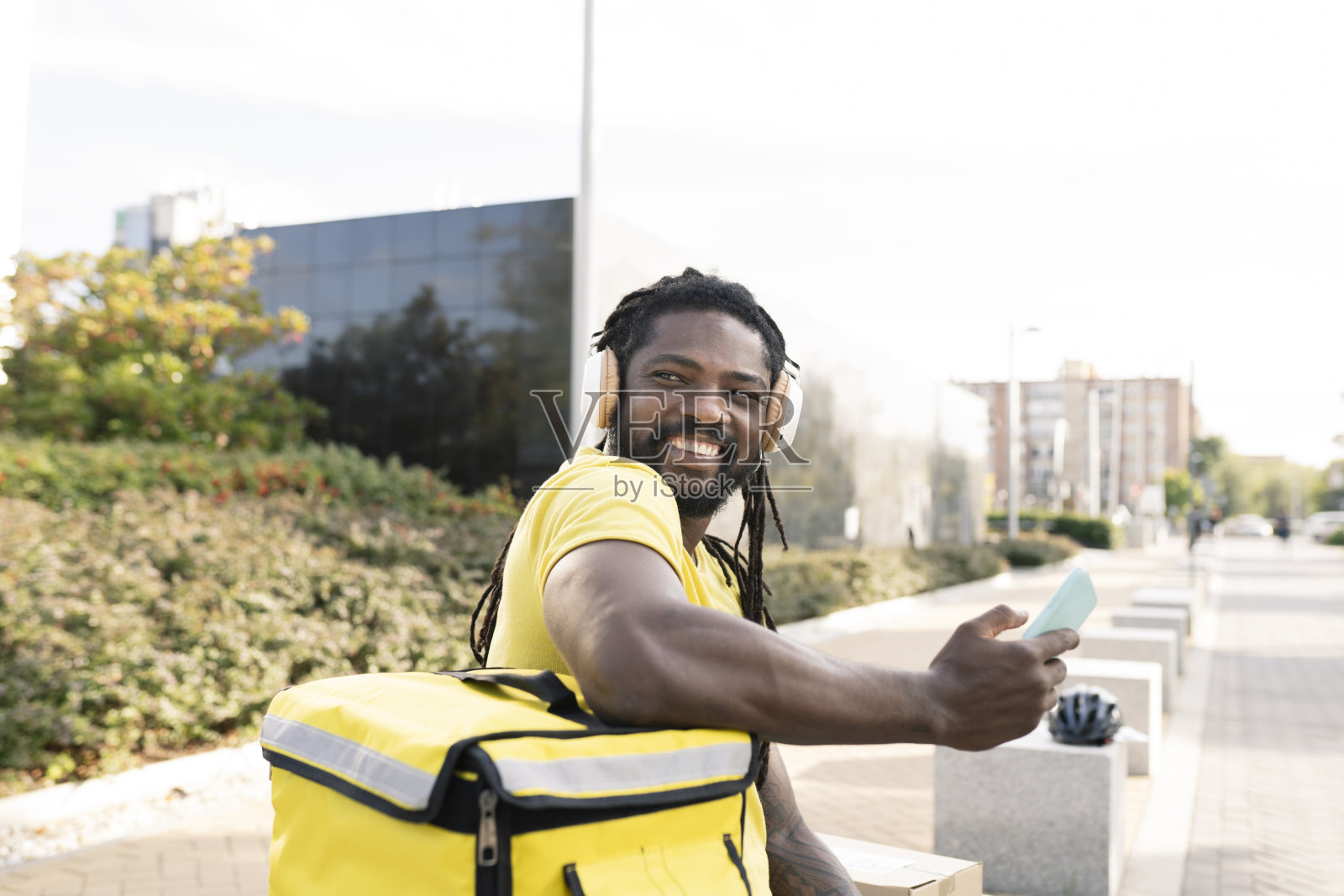 穿着黄色制服的年轻西班牙裔送货员带着耳机微笑地听着音乐,从纸盒里拿出一个纸盒。外观。照片摄影图片