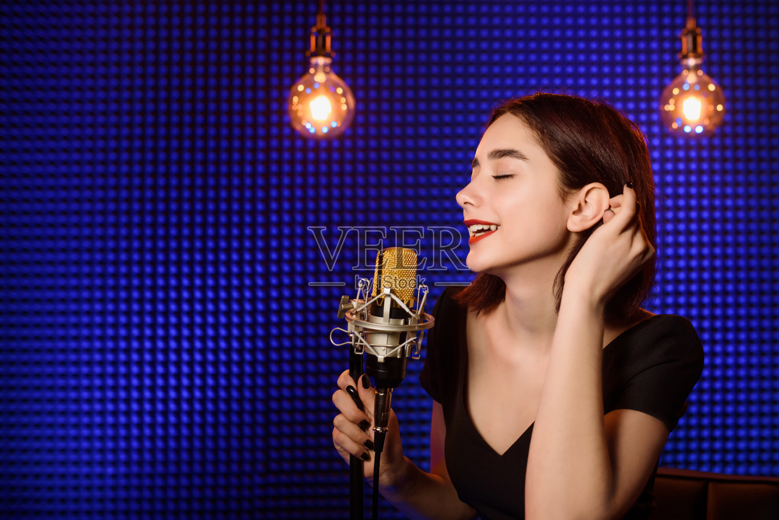 一位年轻的女歌手正在录音室里录制歌曲。照片摄影图片