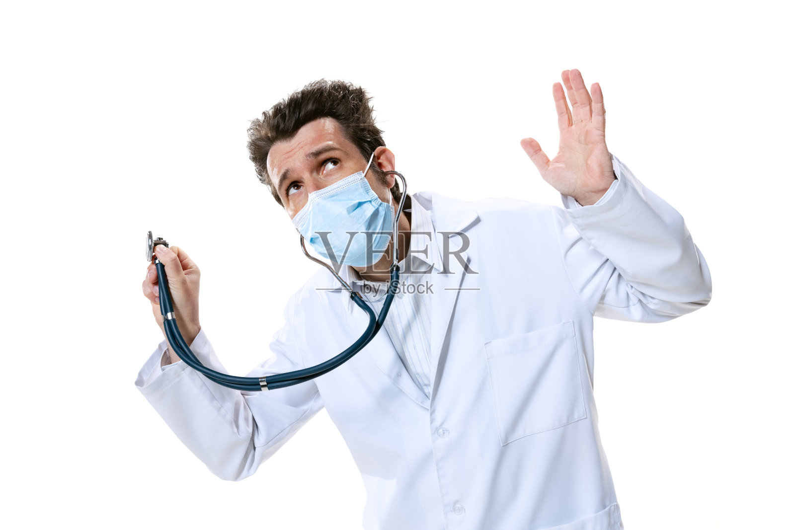 年轻的男性医生,在白色的工作室背景下戴着听诊器和口罩。看起来很难过,认真的。保健和医药的概念,战争,帮助,治疗照片摄影图片
