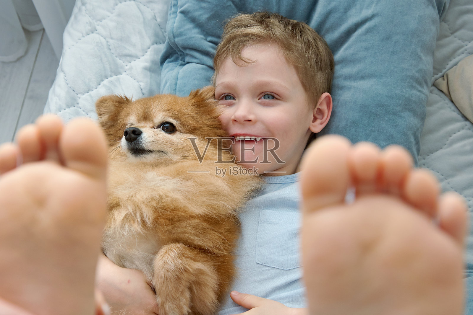 一个微笑的金发孩子,和一只毛茸茸的红狗玩耍,拥抱他的宠物。照片摄影图片