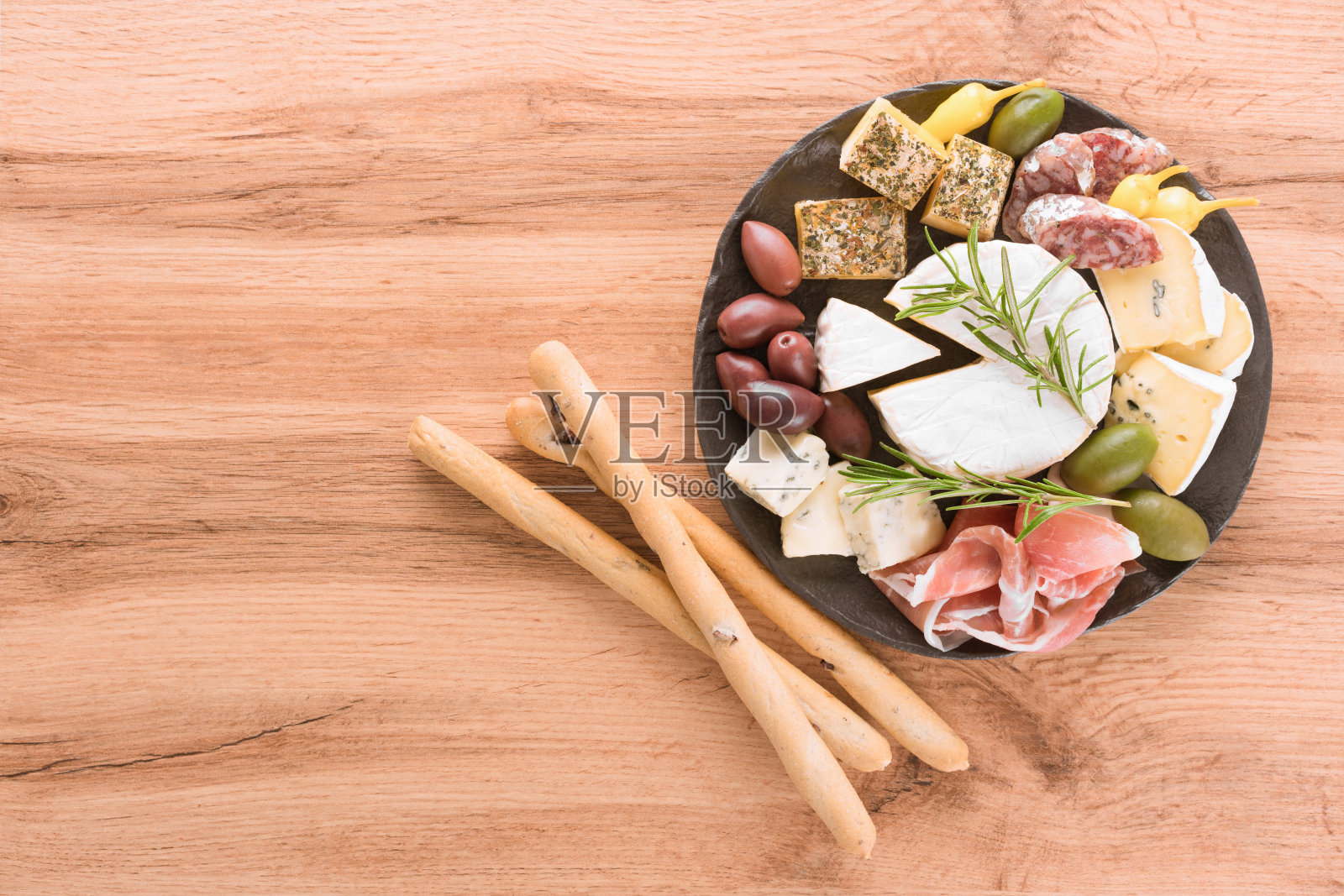 熟食板与选择的奶酪,香肠和熏火腿一起服务橄榄和面包棒在木制的桌子上的黑色盘子。意大利传统开胃菜,俯视图照片摄影图片