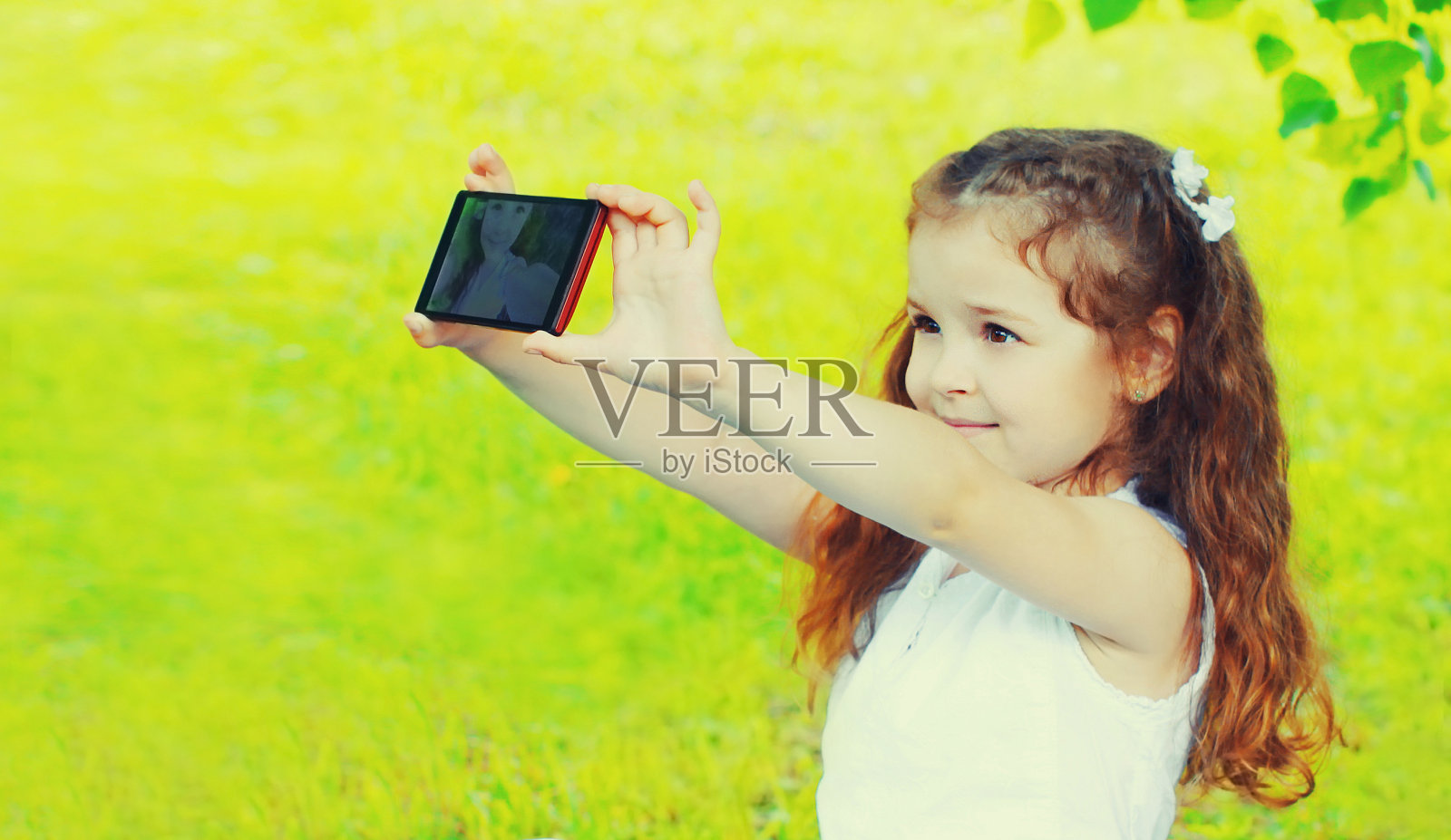 在夏天的公园里,快乐微笑的小女孩用智能手机自拍照片摄影图片