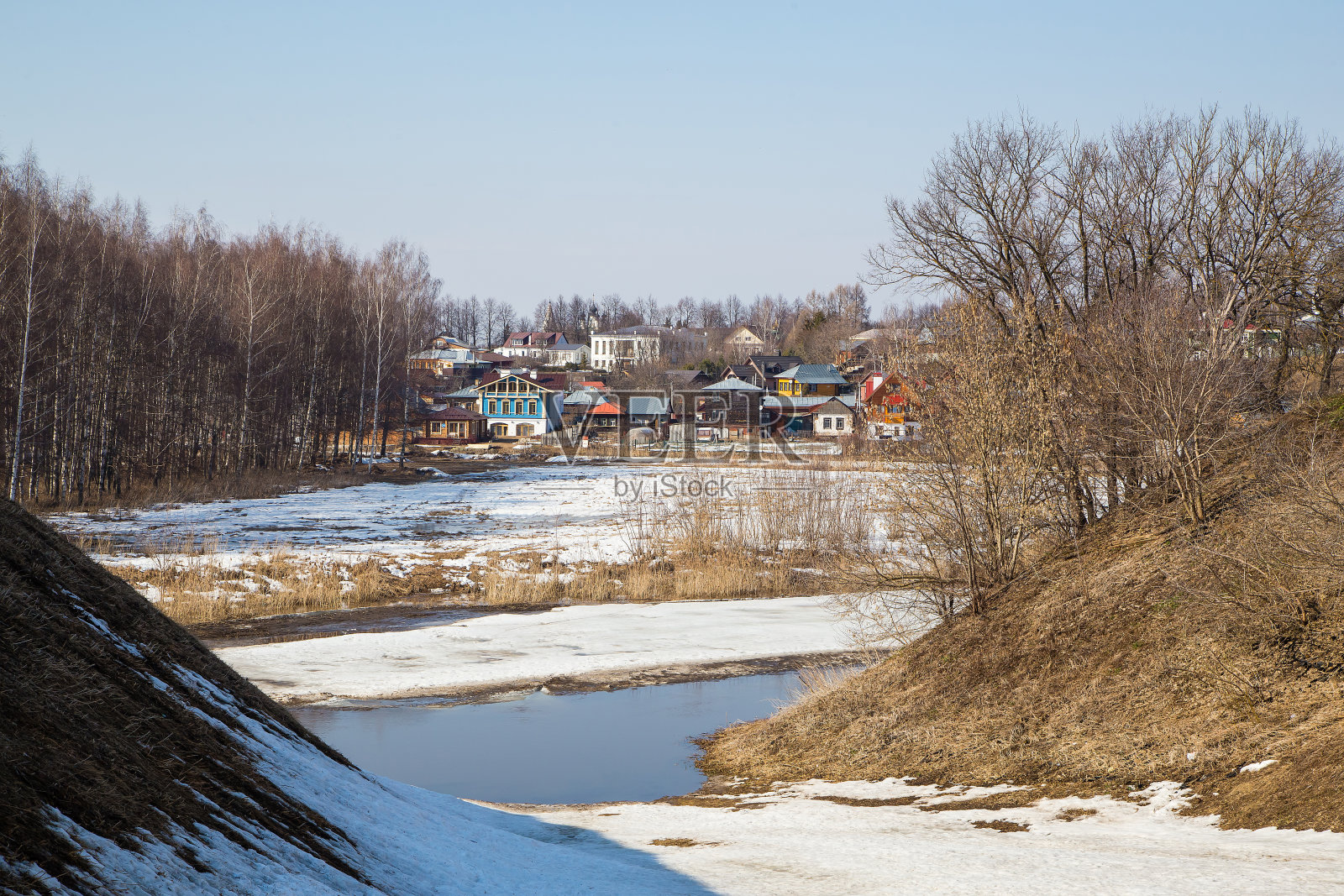 一条结冰的河流延伸到远处,远处是木屋。照片摄影图片