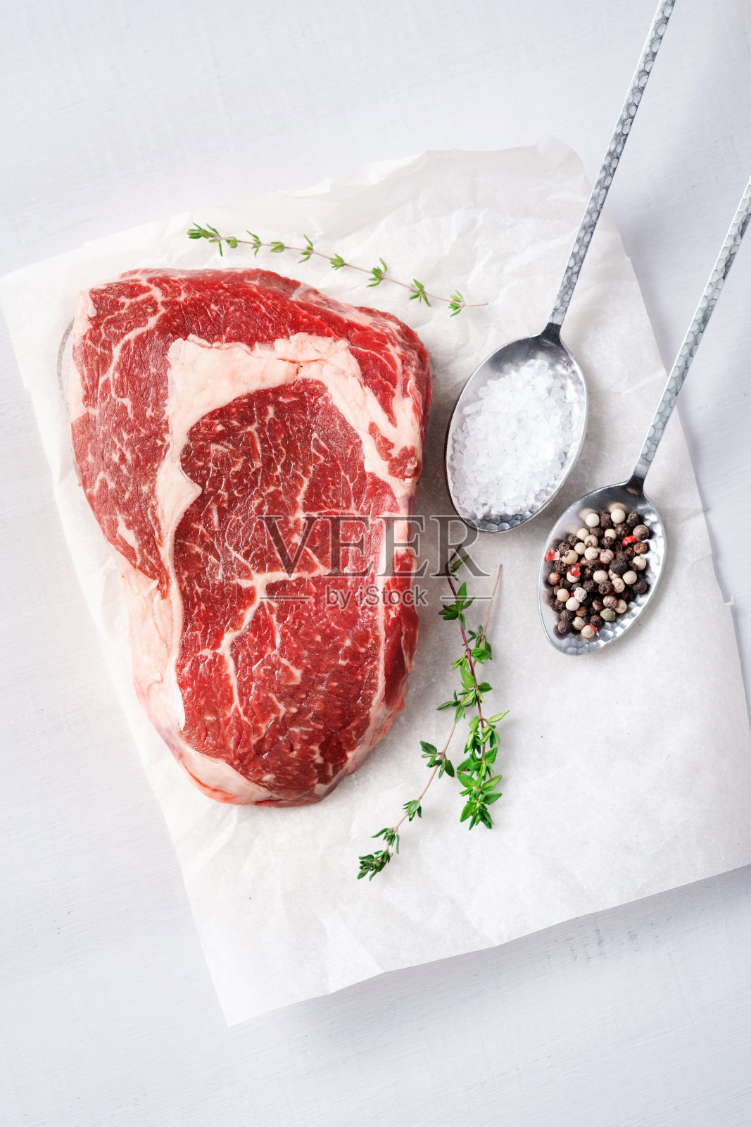 生肋排眼牛排在白色烘烤纸与盐和香草,俯视图照片摄影图片