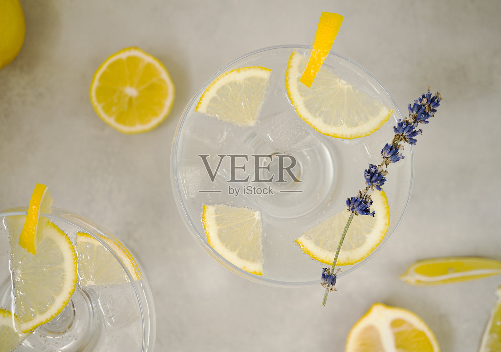 清水和柠檬片放在浅灰色的混凝土背景上。玻璃上装饰着一支薰衣草枝和一片柠檬。旁边是切片的柠檬。俯视图,特写照片摄影图片