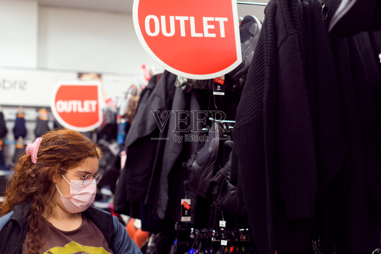 真实的,戴着防护口罩的年轻女子在一家折扣店买衣服。照片摄影图片