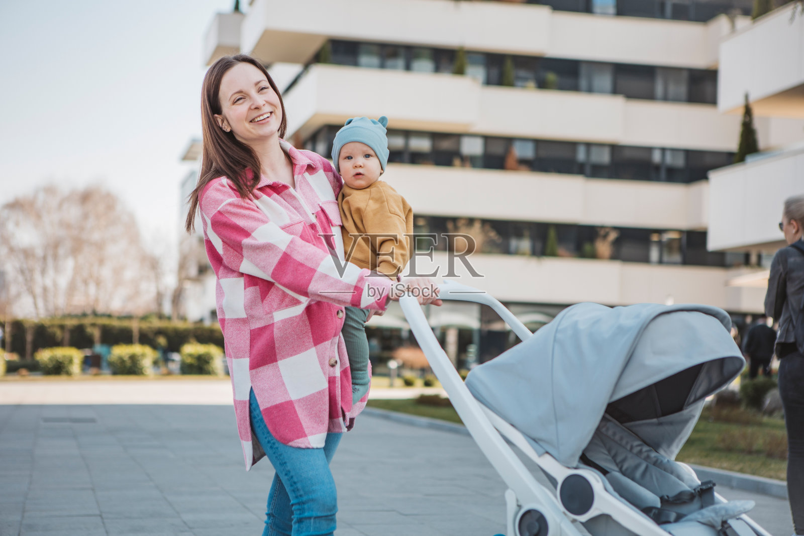 年轻的妈妈抱着婴儿,推着现代的婴儿车,漫步在城市中照片摄影图片