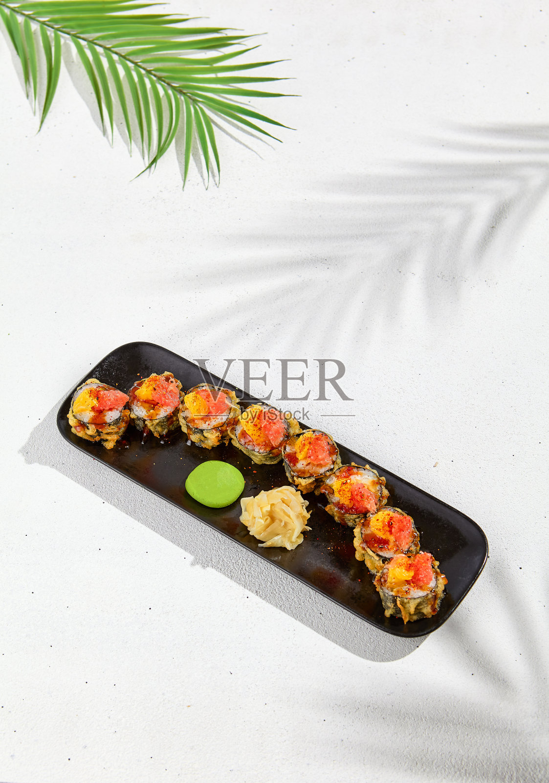 柚子芒果酱天妇罗寿司卷。热maki寿司在黑色盘子上的白色背景。日本料理的夏季菜单。带有硬阴影和树叶的现代寿司菜单。照片摄影图片