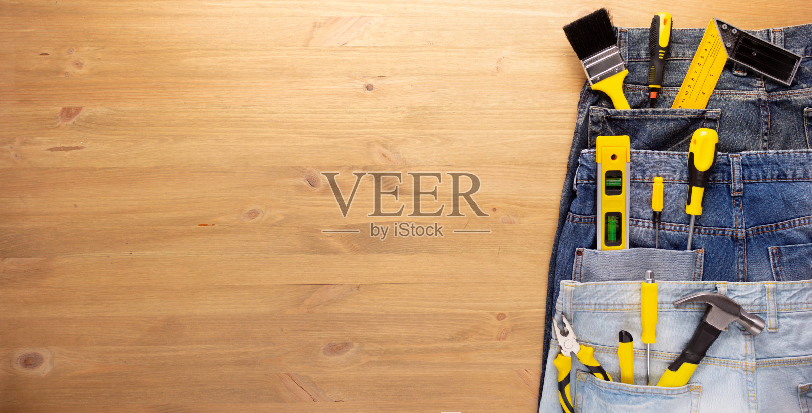 在木制桌子背景的牛仔裤口袋里的工具套件。房子装修的概念照片摄影图片