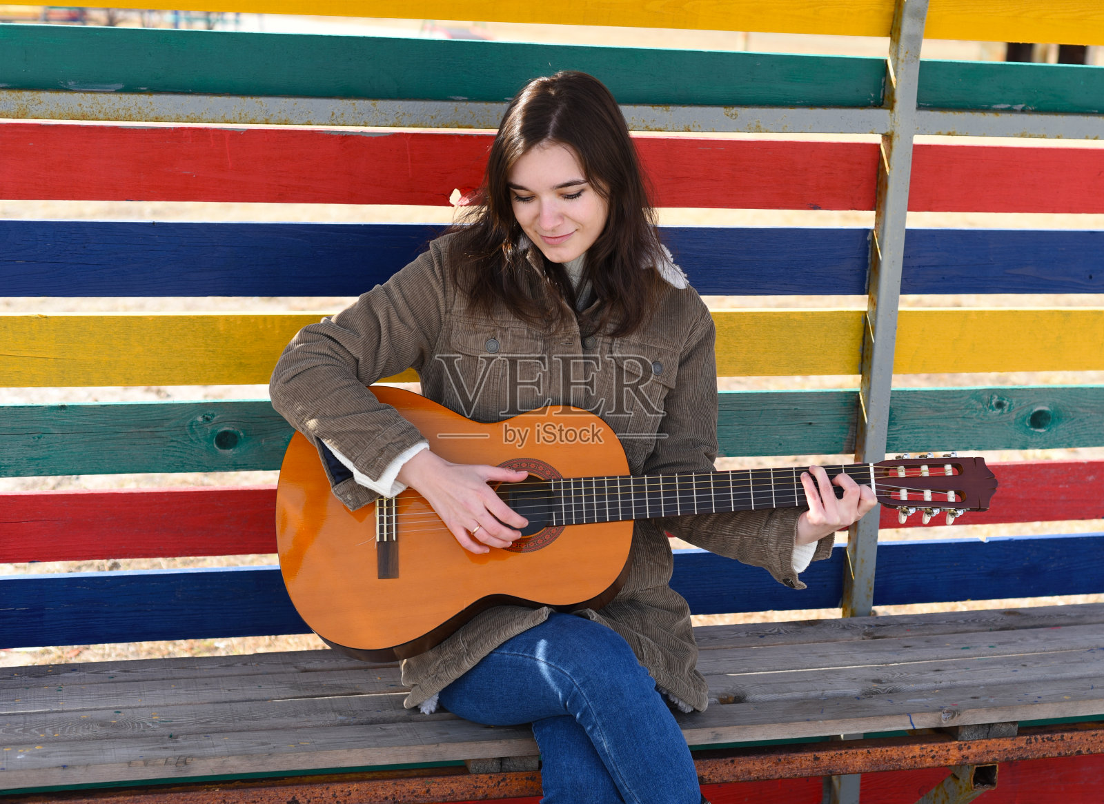 年轻女子弹着吉他,笑着,坐在彩色背景的长椅上照片摄影图片