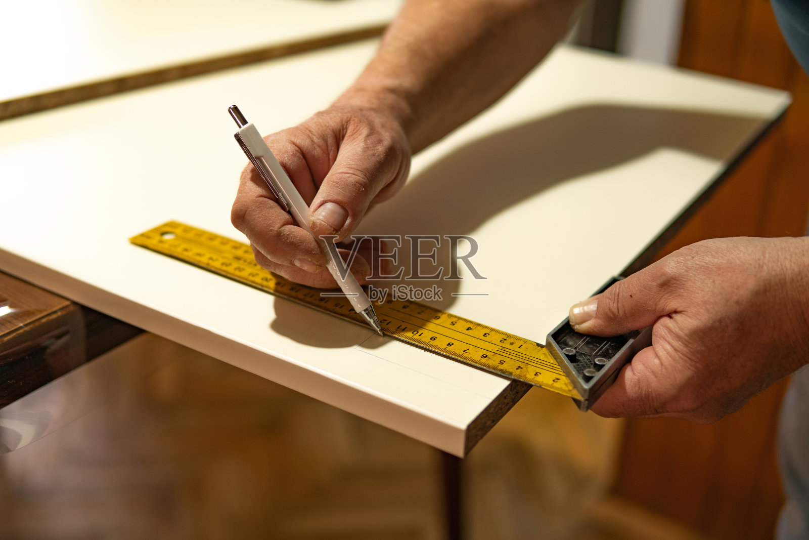 近距离观察,人类的双手用尺子测量并在一块木板(胶合板)上做记号,为自己的家做家具。在家DIY项目。照片摄影图片
