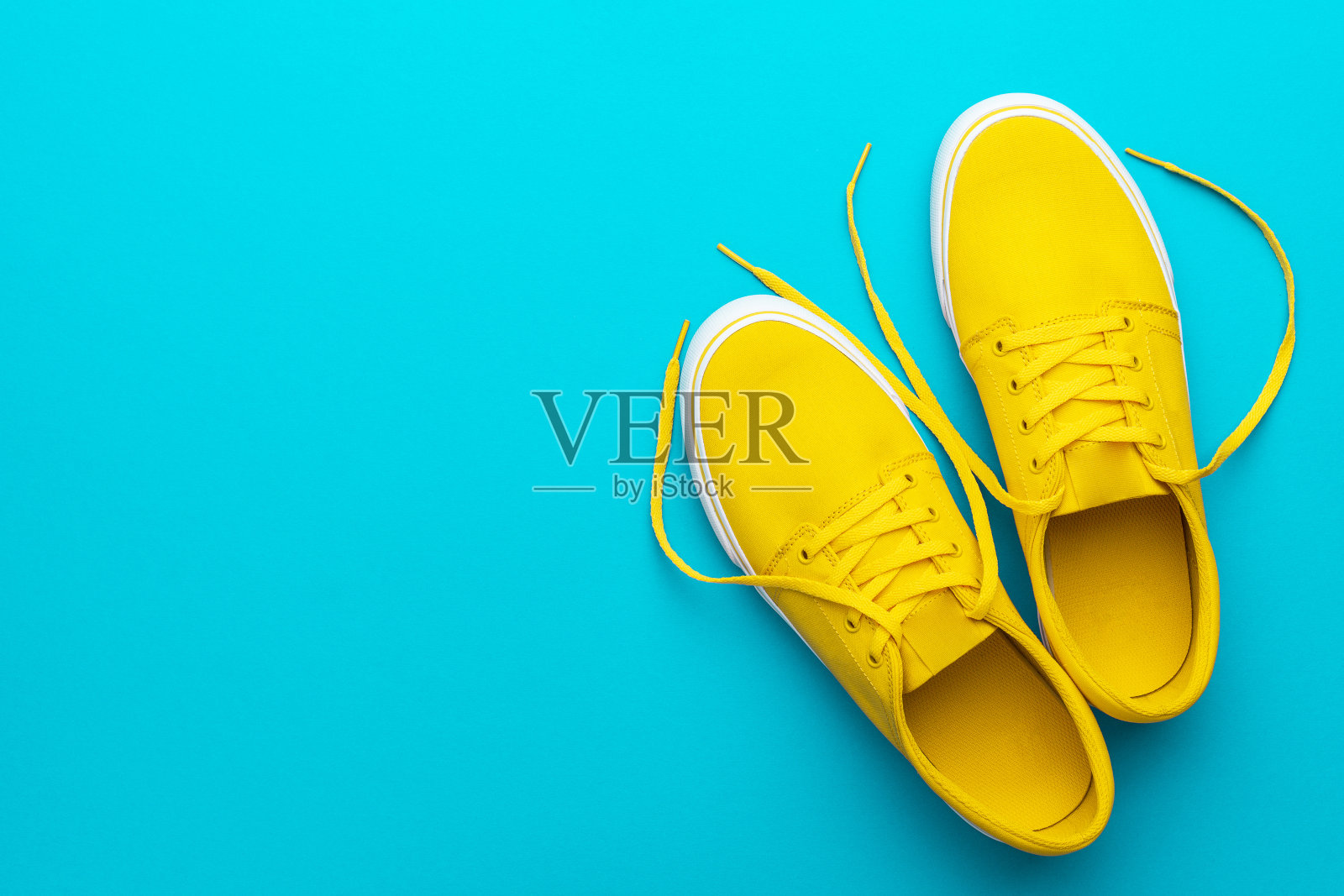 在蓝色绿松石色背景与复制空间上黄色解开运动鞋的俯视图照片摄影图片