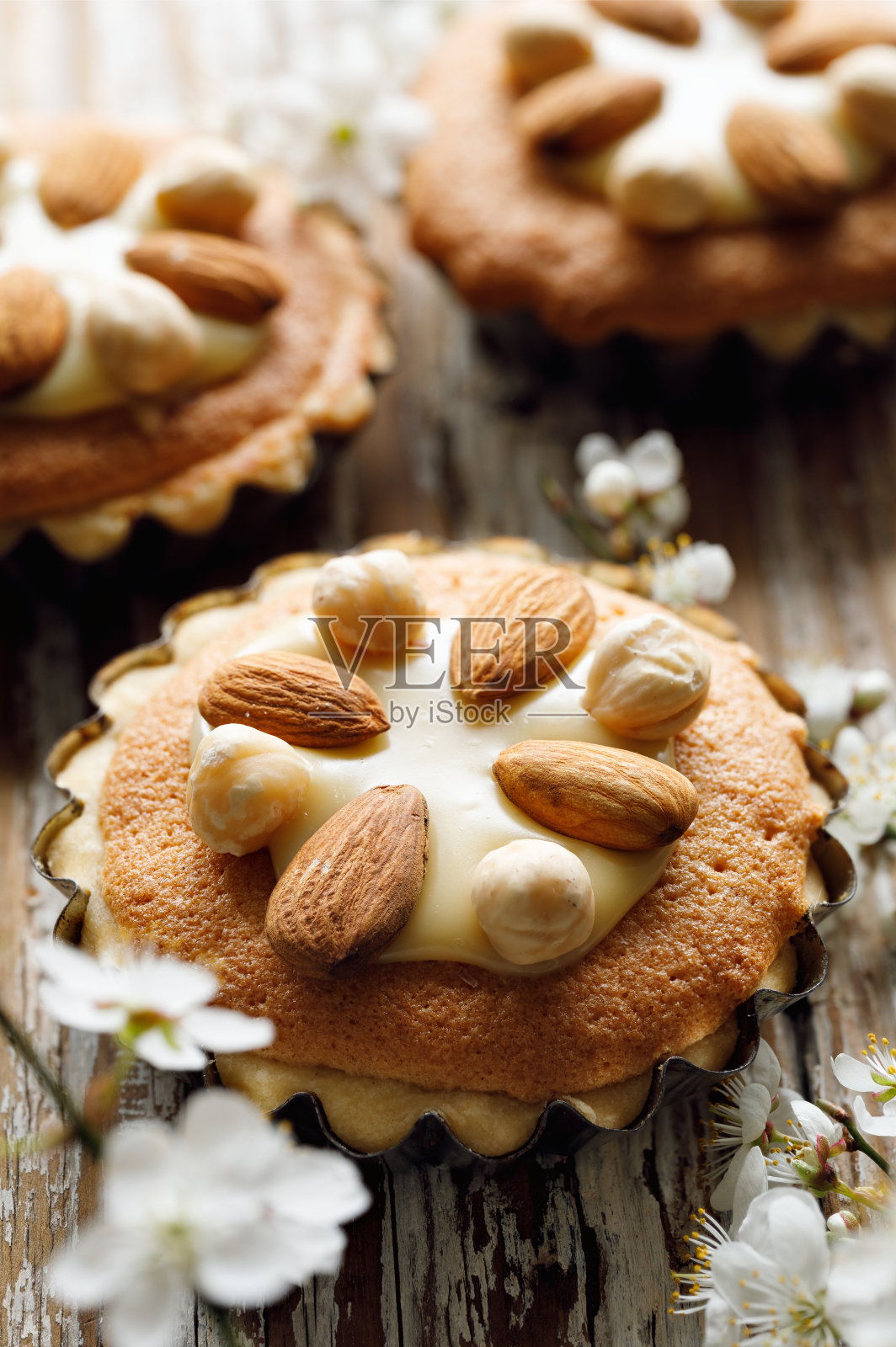在用春天的花朵装饰的木桌上,可以近距离看到迷你挞,上面有杏仁奶油、白巧克力和坚果照片摄影图片