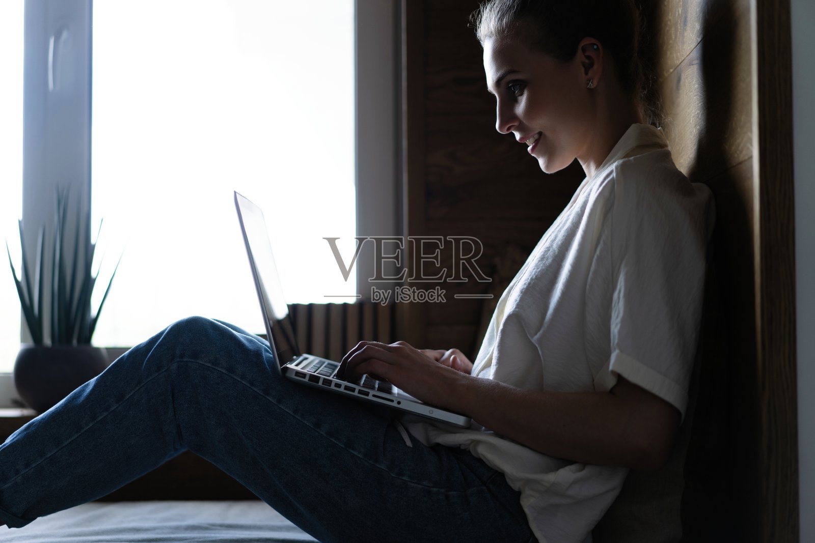 一个穿着休闲的年轻女子坐在家里的窗台上用笔记本电脑工作照片摄影图片