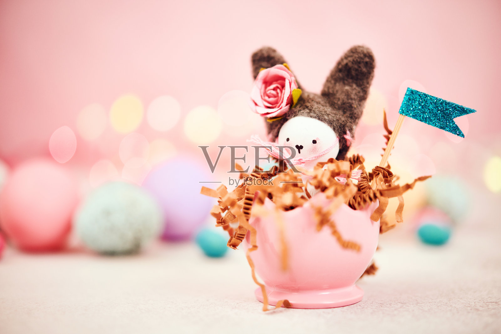 可爱的手工制作的复活节兔子在一个蛋杯里面,周围是复活节彩蛋和粉红色的背景照片摄影图片
