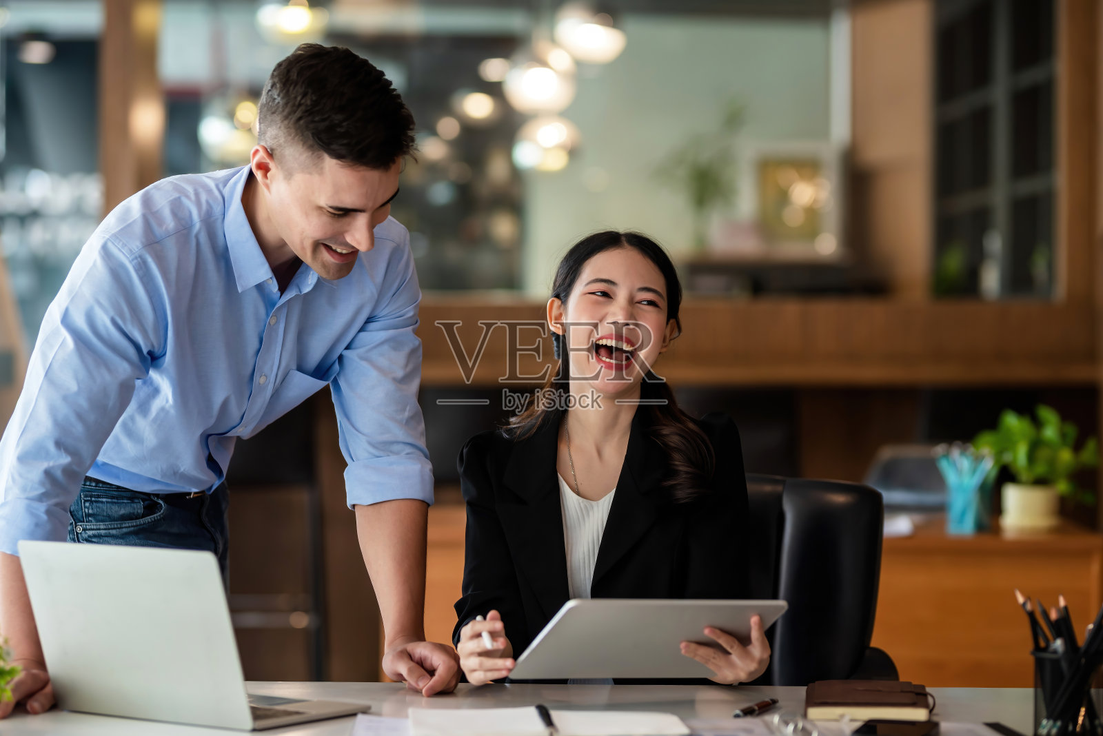 年轻的亚洲女商人开心地笑着,她和同事一起在办公室用平板电脑工作。照片摄影图片