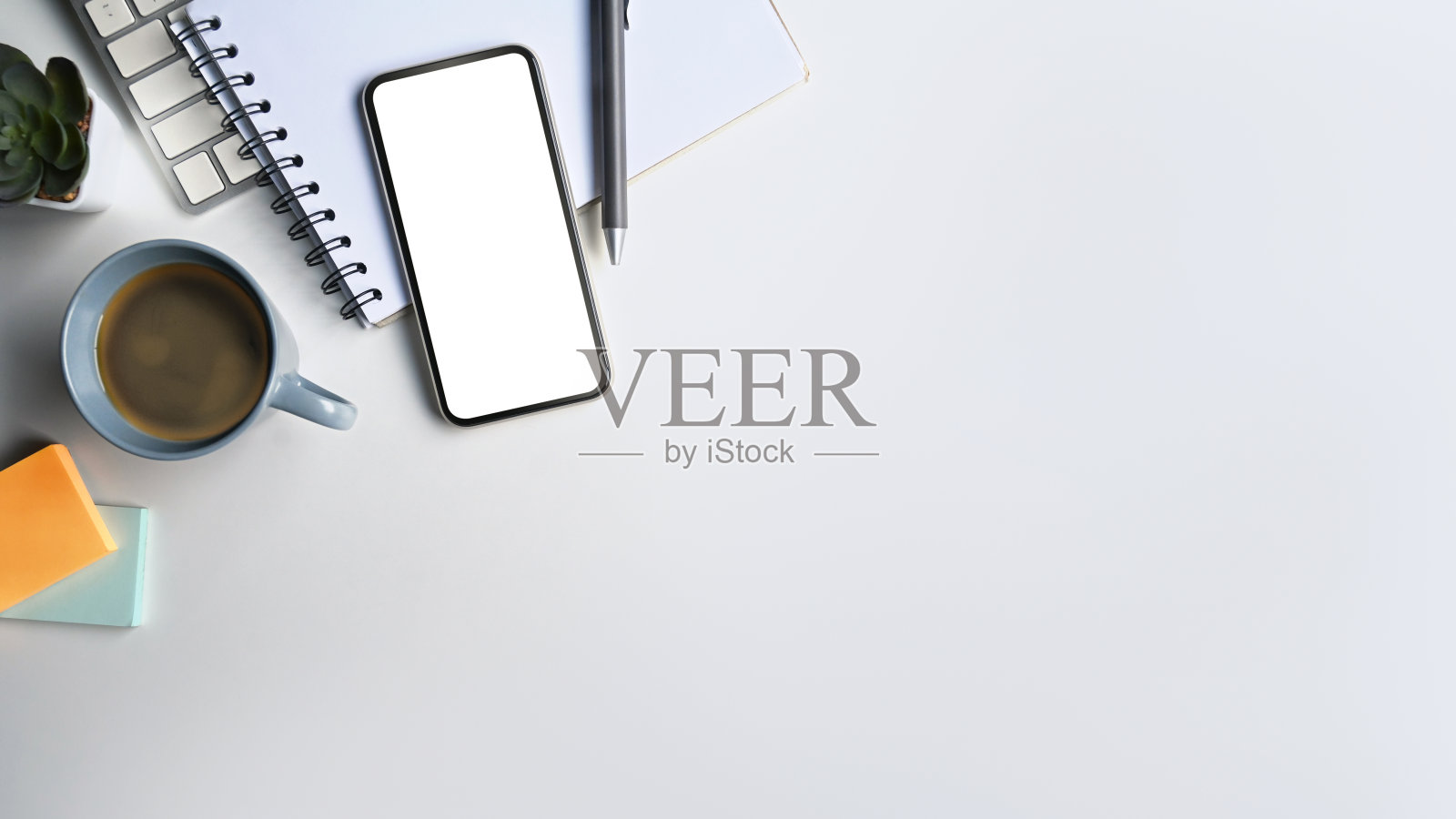 有空白屏幕的手机,有复印空间的白色桌子上的咖啡杯和笔记本。照片摄影图片