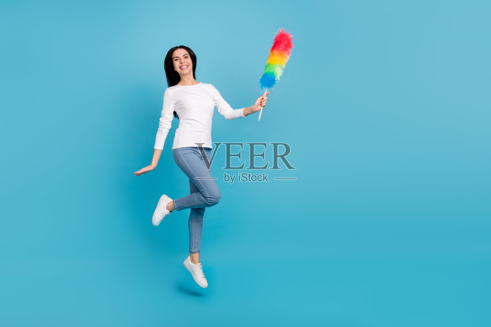 迷人的快乐的女孩女佣跳跃的全长身体尺寸视图使用刷子孤立在明亮的蓝色背景上照片摄影图片