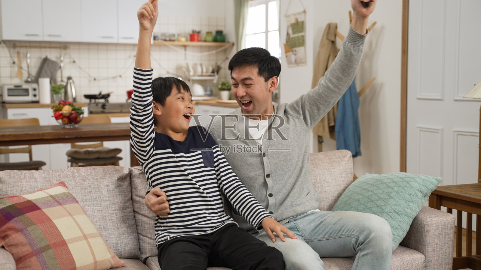 年轻的日本亚洲男子在客厅的沙发上放松与父亲尖叫支持最喜欢的运动队一起。兴奋的成熟的爸爸和上学的儿子休息在家里看电视足球比赛照片摄影图片