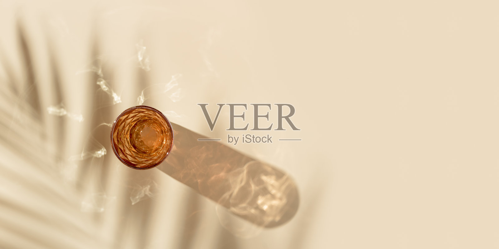 一杯水从彩色玻璃和美丽的阴影从棕榈叶和炫目的阳光,夏季饮料的概念,趋势玻璃橙色,米色背景,审美俯视图照片摄影图片