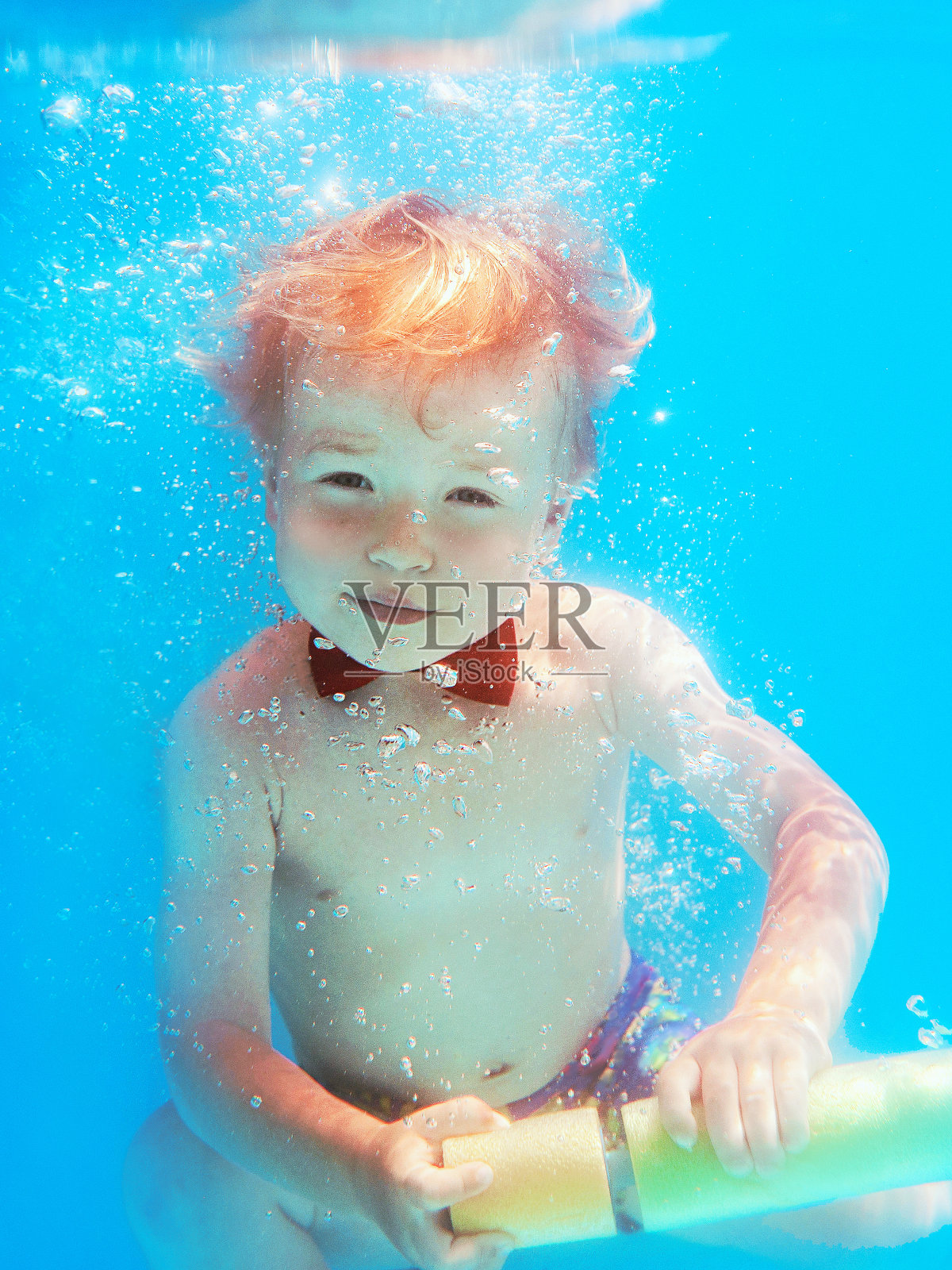 小男孩婴儿带着红蝴蝶在游泳池潜泳,学习游泳。运动与度假概念照片摄影图片