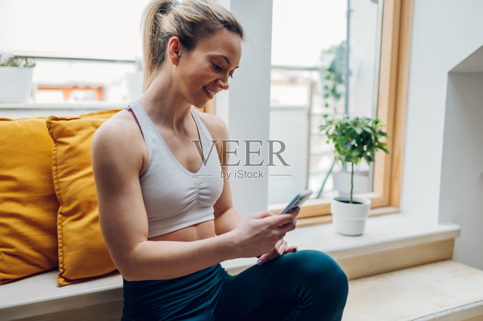 在家训练后坐在窗台上使用智能手机的女人照片摄影图片