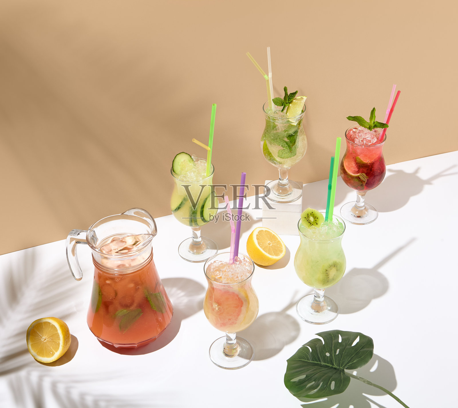 白色的桌子上有一组柠檬水和排毒饮料。夏天喝的概念。米色墙壁和白色桌子与阳光和手掌阴影。柠檬水设置菜单。照片摄影图片