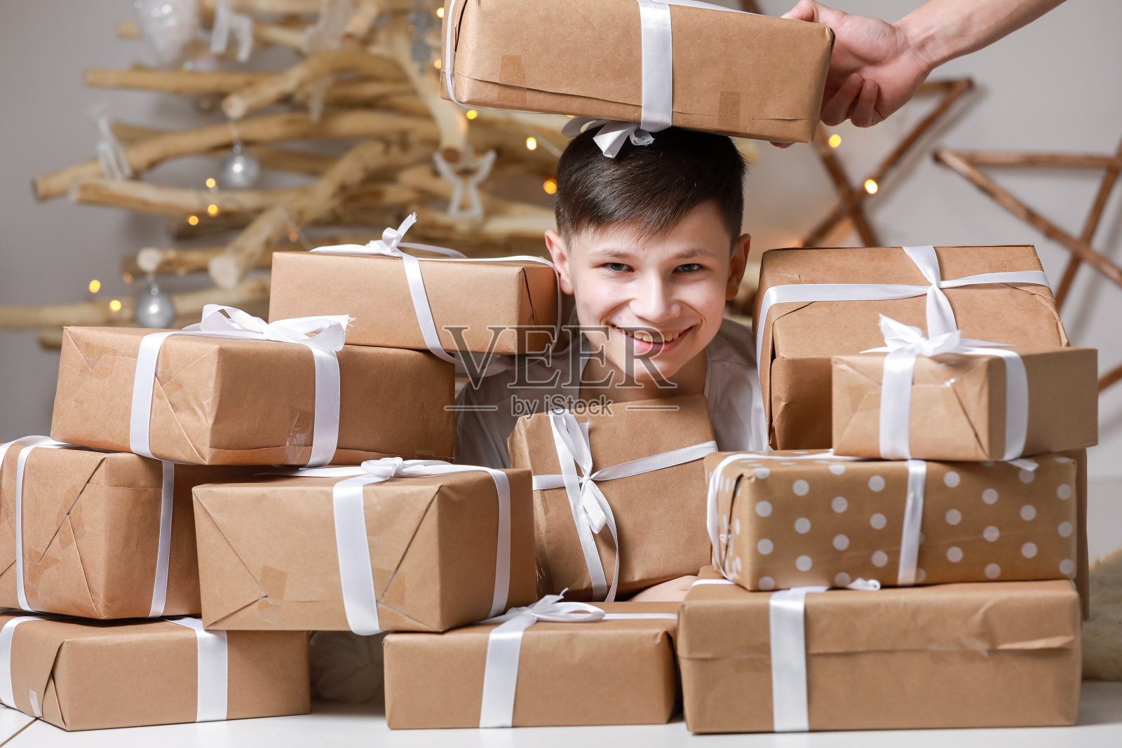 假日购物。孩子在圣诞树旁庆祝节日。面带微笑的十几岁的男孩正在玩很多礼品盒。新年快乐。装饰圣诞树。照片摄影图片