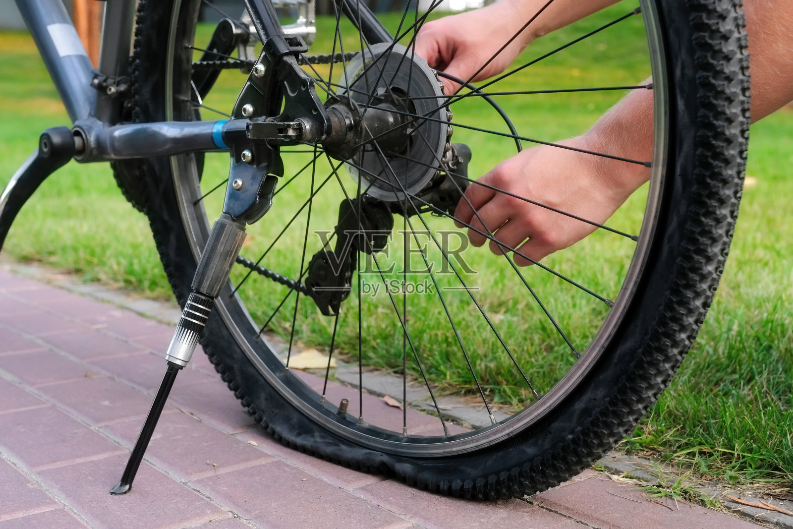 一个年轻人在公园里修理一辆自行车的后轮。自行车维修保养照片摄影图片