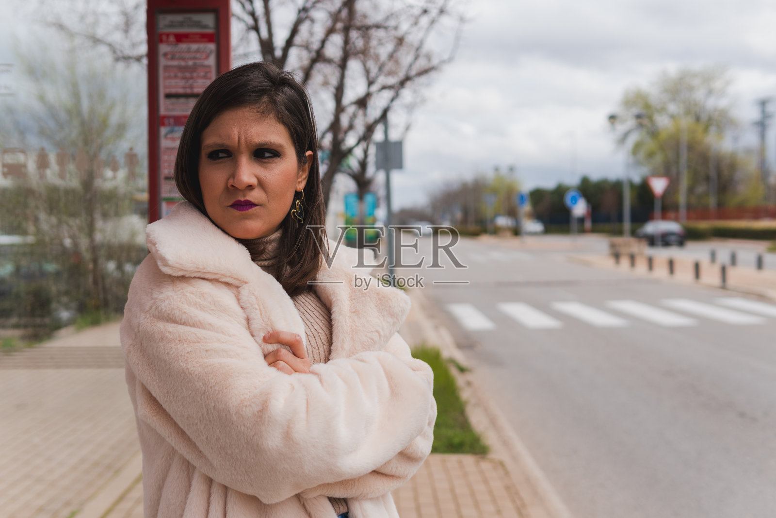 在公共汽车站等公共交通工具时面带怒气的女人。照片摄影图片