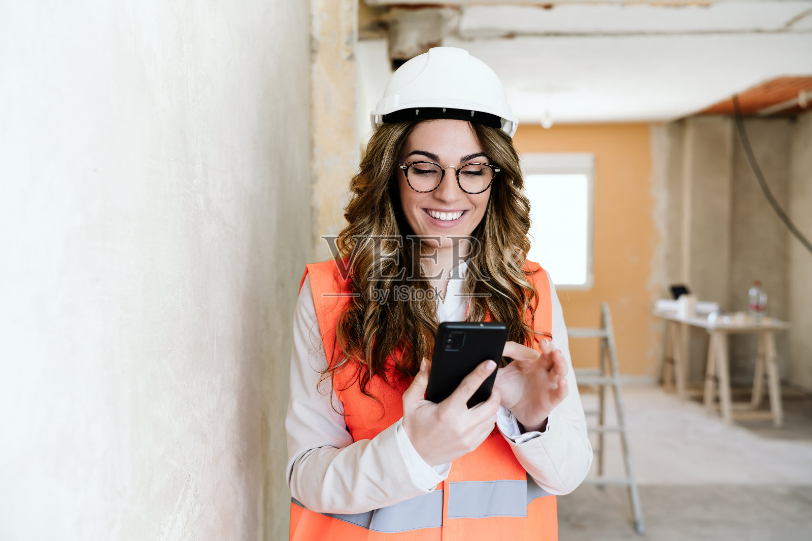 专业女建筑师在施工现场使用手机和图纸。家里装修照片摄影图片
