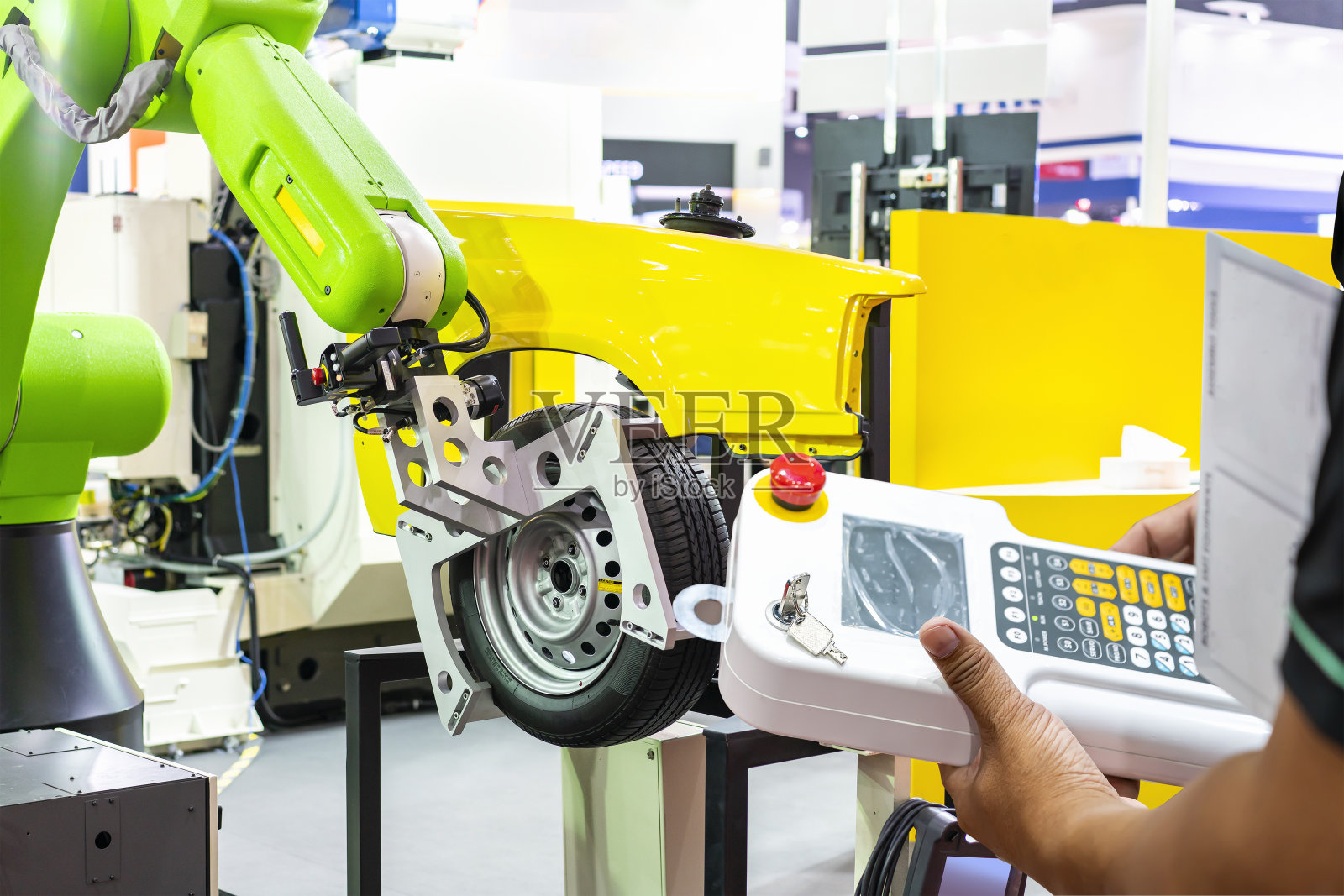 制造过程中,人工技术人员输入程序命令或操作机器人,通过无线遥控抓手,控制车轮轮胎与汽车结构的模拟装配照片摄影图片