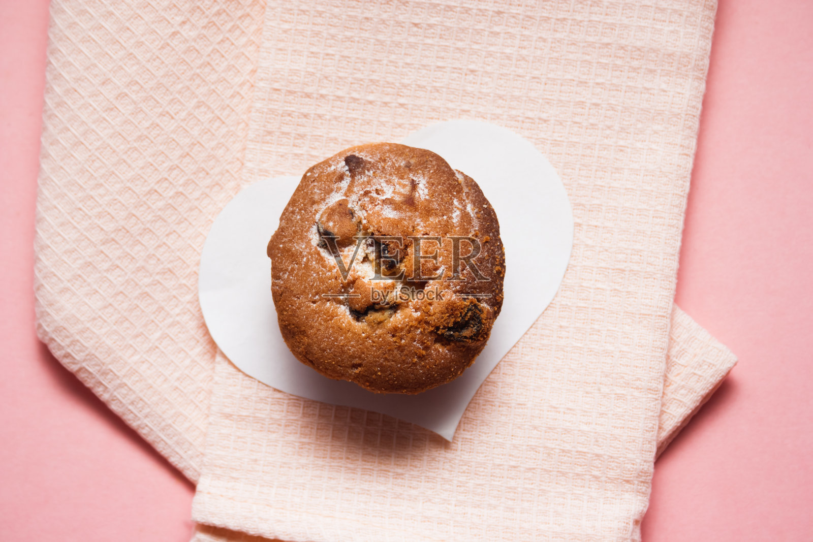 一个有葡萄干的纸杯蛋糕,放在白色的心形图案上,上面铺着一条轻毛巾照片摄影图片