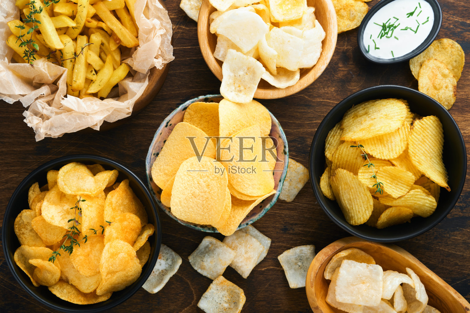 不健康的食物或零食。所有经典的土豆零食,花生,爆米花,洋葱圈和咸椒盐卷饼在碗盘在旧的木制背景。对身材,心脏,皮肤,牙齿都不健康的食物。照片摄影图片