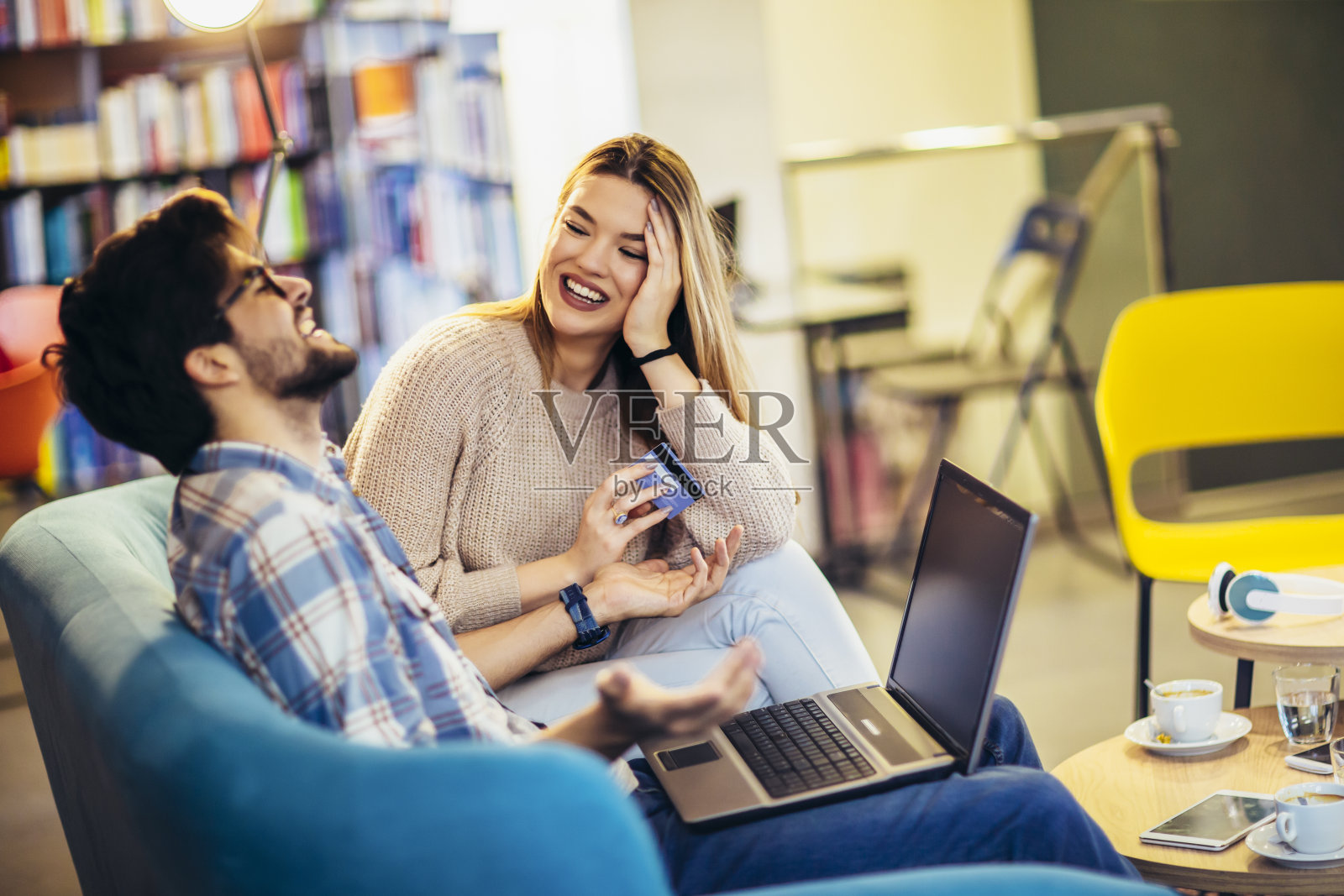 漂亮的年轻夫妇带着笔记本电脑在咖啡馆,他们用信用卡在网上购物。照片摄影图片