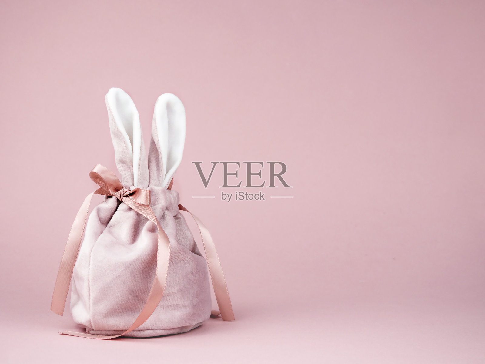 粉色背景上有兔子耳朵的粉色袋子。复活节的概念,一份礼物照片摄影图片
